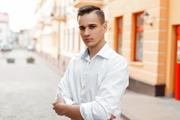 Bonito homem elegante com um corte de cabelo em uma camisa branca cruzou os braços na cidade — Fotografia de Stock