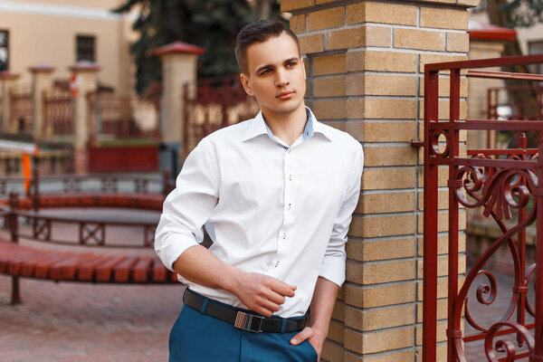 Stylish young man in a white shirt near a brick wall