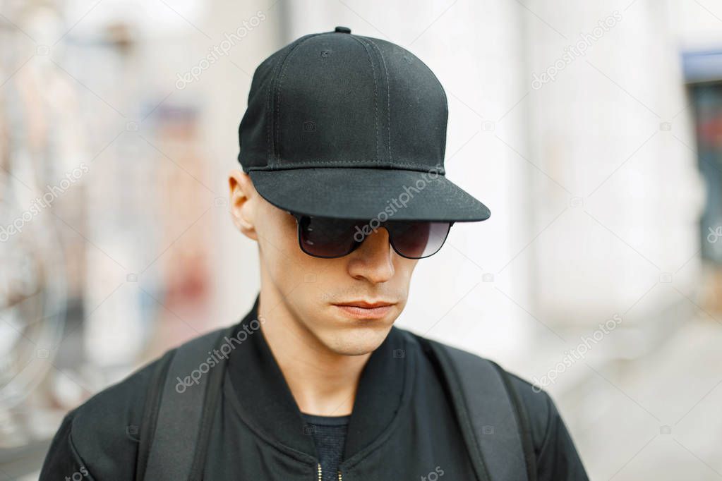 Handsome guy in a black baseball cap and stylish black clothes, outdoors