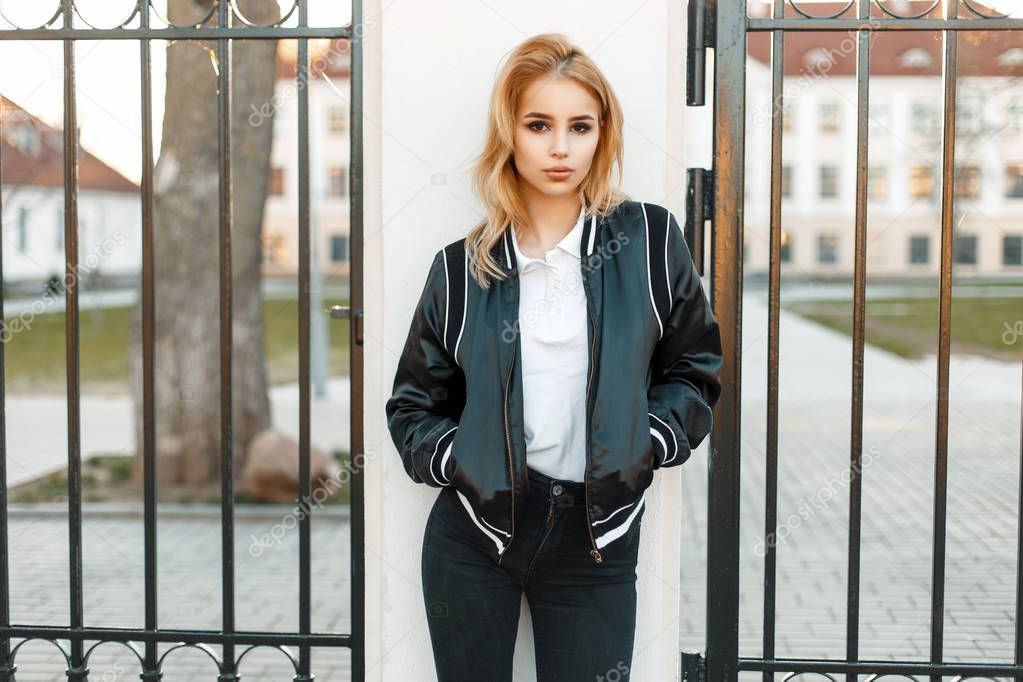 Young girl student in black jacket in college near a fence