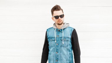 Moda ahşap duvar yakınındaki güneş gözlüklü bir kot yelek erkekte
