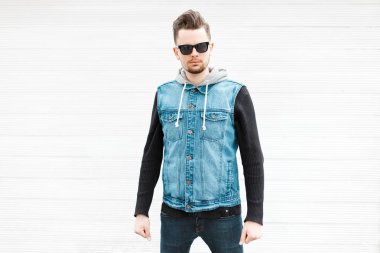 Güneş gözlüğü ve bir beyaz tahta duvarının yakınında şık denim ceket yakışıklı hipster adam