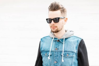 Güneş gözlüğü ve denim yelek duvarın yanında genç bir adam portresi