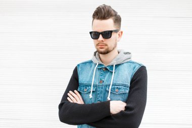 Beyaz ahşap duvara yakın poz güneş gözlüğü ile kot pantolon giysili şık adam