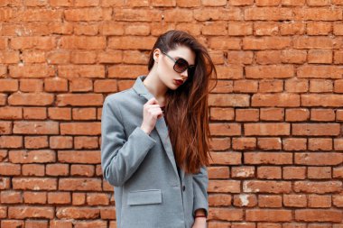 Kırmızı tuğla duvar yakınındaki gri paltolu güneş gözlüklü genç güzel kız
