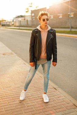 Genç yakışıklı bir siyah deri ceket ve beyaz ayakkabı gün batımında güneş gözlüklü olan