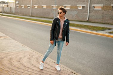 Bununla birlikte güneş gözlüklü bir deri ceket, kot ve road yakınındaki beyaz spor ayakkabı moda yakışıklı delikanlı