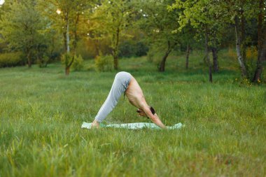 Genç adam parkta yoga yapıyor.