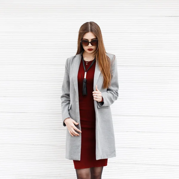 Beautiful young woman in a gray coat and sunglasses near a vintage wooden wall — Stock Photo, Image