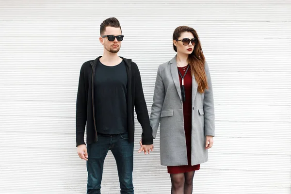 Beautiful fashionable couple of models in stylish clothes near a white vintage wooden wall