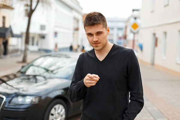 Молодий чоловік у чорній футболці вказує пальцем на вулицю — стокове фото