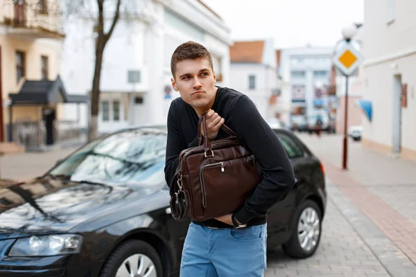 Молодий чоловік вкрав шкіряну сумку на тлі автомобіля — стокове фото