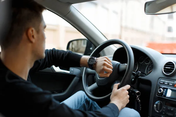 Kierowca-mężczyzna siedzi w samochodzie w korku i patrząc na zegarek — Zdjęcie stockowe