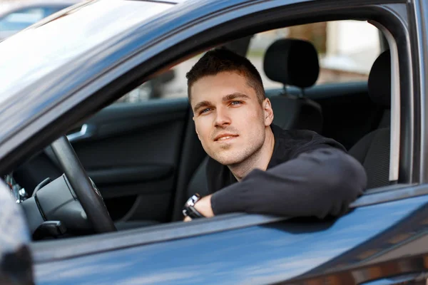 Jovem feliz sentado em um carro preto — Fotografia de Stock