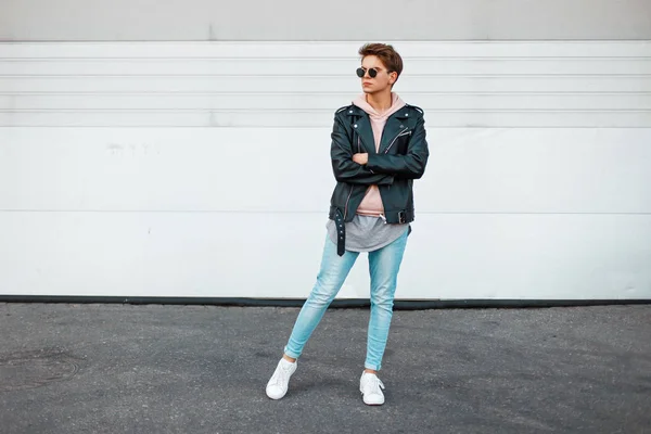 Modelo joven guapo con un peinado en ropa de marca de moda cerca de la puerta de metal blanco — Foto de Stock