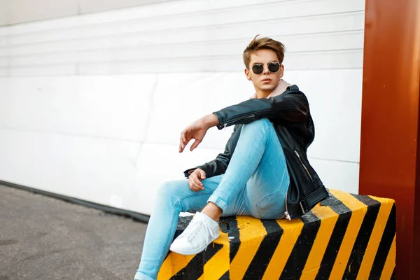 Moda yakışıklı delikanlı markalı şık giysiler içinde siyah ve sarı Beton üzerinde oturur — Stok fotoğraf