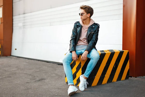 Jovem bonito com um penteado na moda roupas elegantes senta-se em um preto-e-amarelo — Fotografia de Stock