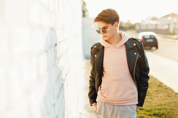 Beau jeune homme à la mode dans une veste en cuir et un sweat rose près d'un mur blanc — Photo