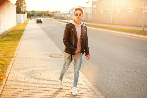 Jóképű férfi egy fekete bőr kabát és fehér cipők, séta az utcán, a naplemente — Stock Fotó