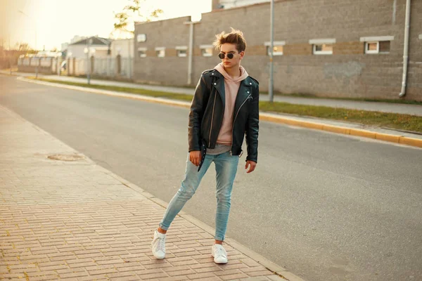 Jovem modelo cara em uma jaqueta de couro preto, uma camisola rosa, jeans e tênis brancos posando na rua — Fotografia de Stock