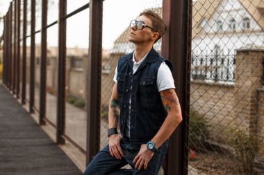 Yakışıklı genç adam bir saç modeli ve bir kot yelek ızgarayı yakın gözlük ile