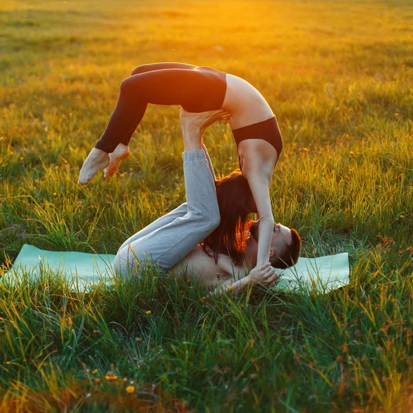 Молода пара робить йогу поза містом на траві на заході сонця — стокове фото