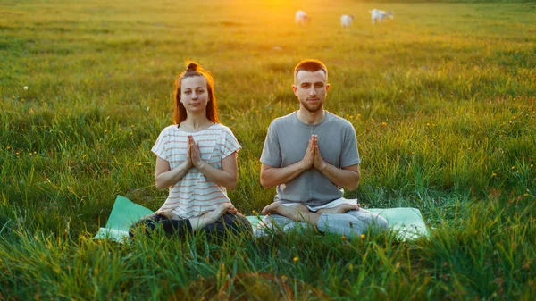 Young couple practicing yoga outdoors at sunset — Stock Photo, Image