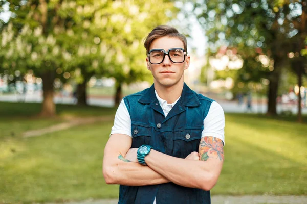 Portrait d'un beau jeune homme avec des lunettes vintage et des vêtements de jeans lors d'une journée d'été ensoleillée dans le parc — Photo