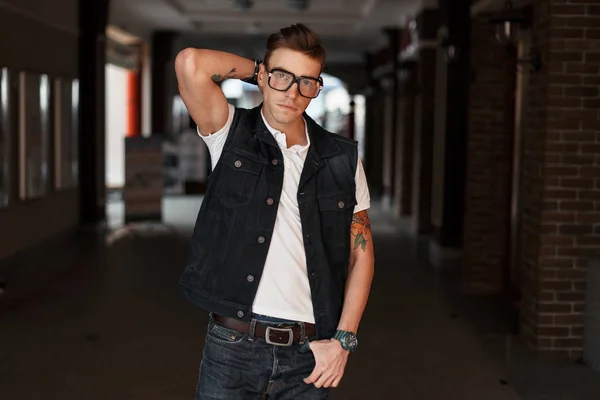 Jeune homme beau avec des lunettes dans un gilet en jean et un T-shirt blanc dans la rue — Photo