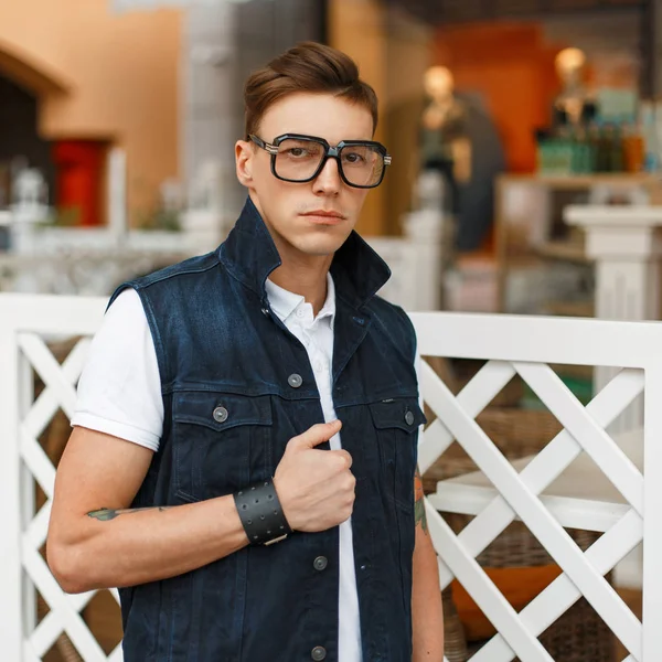 Стильний молодий чоловік в старовинних окулярах і джинсових прогулянках жилетом в торговому центрі — стокове фото