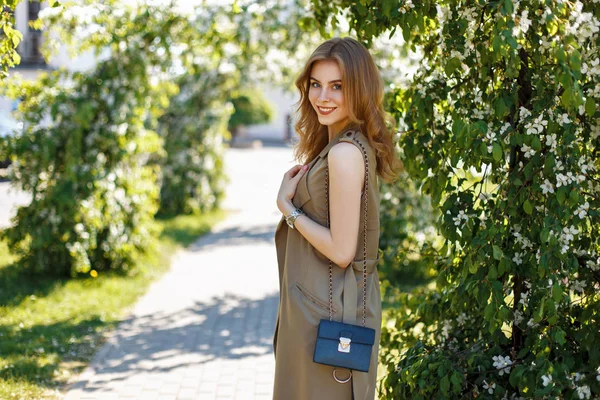 Giovane donna felice con un sorriso in abiti eleganti con una borsa in una giornata di primavera nel parco — Foto Stock