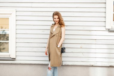 Oldukça mutlu kadın moda giysiler bir ahşap duvarının yakınında bir el çantası ile bir gülümseme