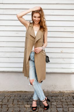 Kot ile modern giyimleri ve ahşap kereste duvarının yakınında bir el çantası siyah ayakkabılarla bir gülümseme mutlu genç kadın