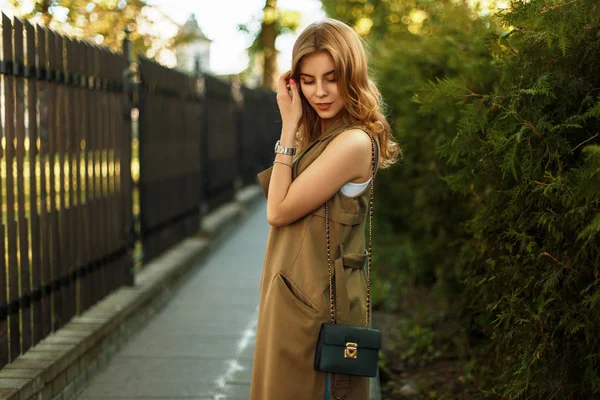 Hermosa joven con un bolso de mano en ropa de moda caminando al aire libre —  Fotos de Stock