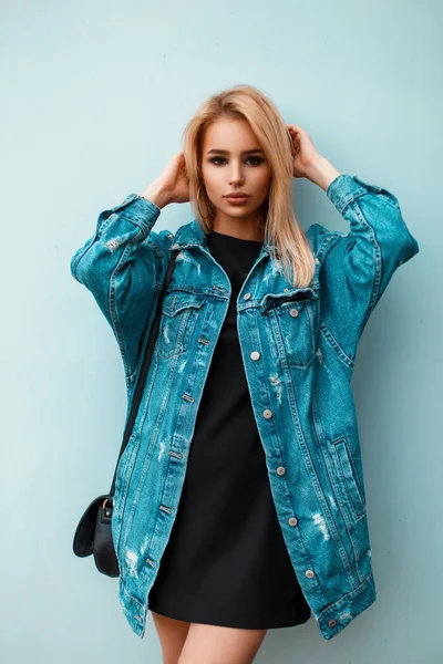 Mulher loira bonita com bolsa em roupas de ganga azul posando perto da parede azul — Fotografia de Stock