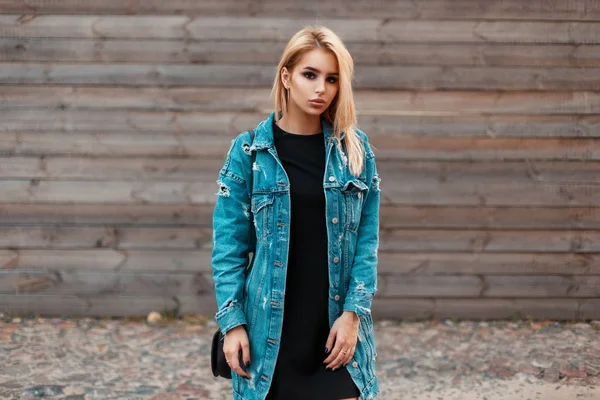 Красивая молодая женщина в модной джинсовой куртке позирует возле винтажной деревянной стены — стоковое фото