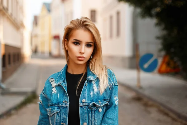 Linda jovem mulher loira elegante em uma jaqueta de jeans na moda na rua — Fotografia de Stock