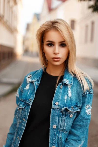 Красива молода дівчина з чистим доглядом за шкірою в джинсах стильний піджак біля будівель на вулиці — стокове фото