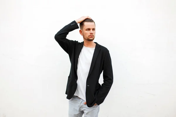 Schöner stylischer junger Mann in trendiger Kleidung in der Nähe einer weißen Wand — Stockfoto