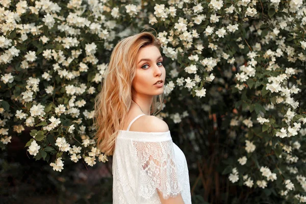 Beautiful young blond woman in vintage white lace T-shirt on nature near bush with flowers — Stock Photo, Image