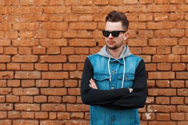 Yakışıklı erkek güneş gözlüğü ve bir tuğla duvar yakınındaki bir kot yelek
