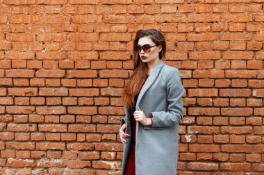 Gri bir ceket ve güneş gözlüğü bir tuğla duvar yakınındaki güzel kadın