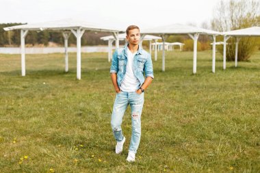 Yakışıklı adam şık denim giyim ve Beyaz tişört, beyaz saçak ile Sahilde yürüyüş spor ayakkabı