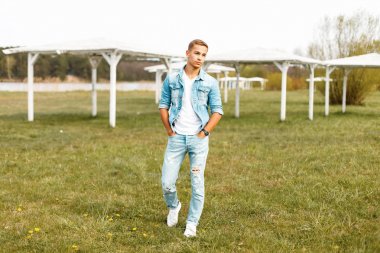 Yakışıklı genç bir kot ceket ve yırtık kot doğada yürüyüş ile beyaz T-shirt