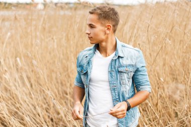 Kot elbise ve Beyaz tişört yakışıklı genç adam açık havada çimenlerde yürüyor