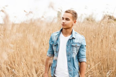 Yakışıklı genç bir beyaz kot ceket T-shirt açık havada çimenlerde yürüyor