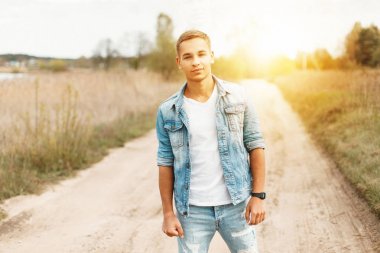 Yakışıklı genç bir kot ceket ve beyaz bir T-shirt batımında doğada yırtık kot pantolon ile