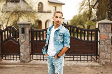 Yakışıklı genç bir şık vintage denim ceket ve çit yakınındaki avluda yırtık kot pantolon