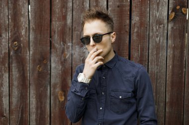 Şık adam sigara içiyor ve darbeler duman bir duvar yakınındaki.