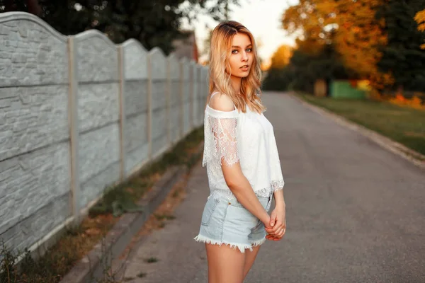 Mooie sexy model blonde vrouw in een witte lace T-shirt met jeans korte broek op een zomerdag in het park — Stockfoto